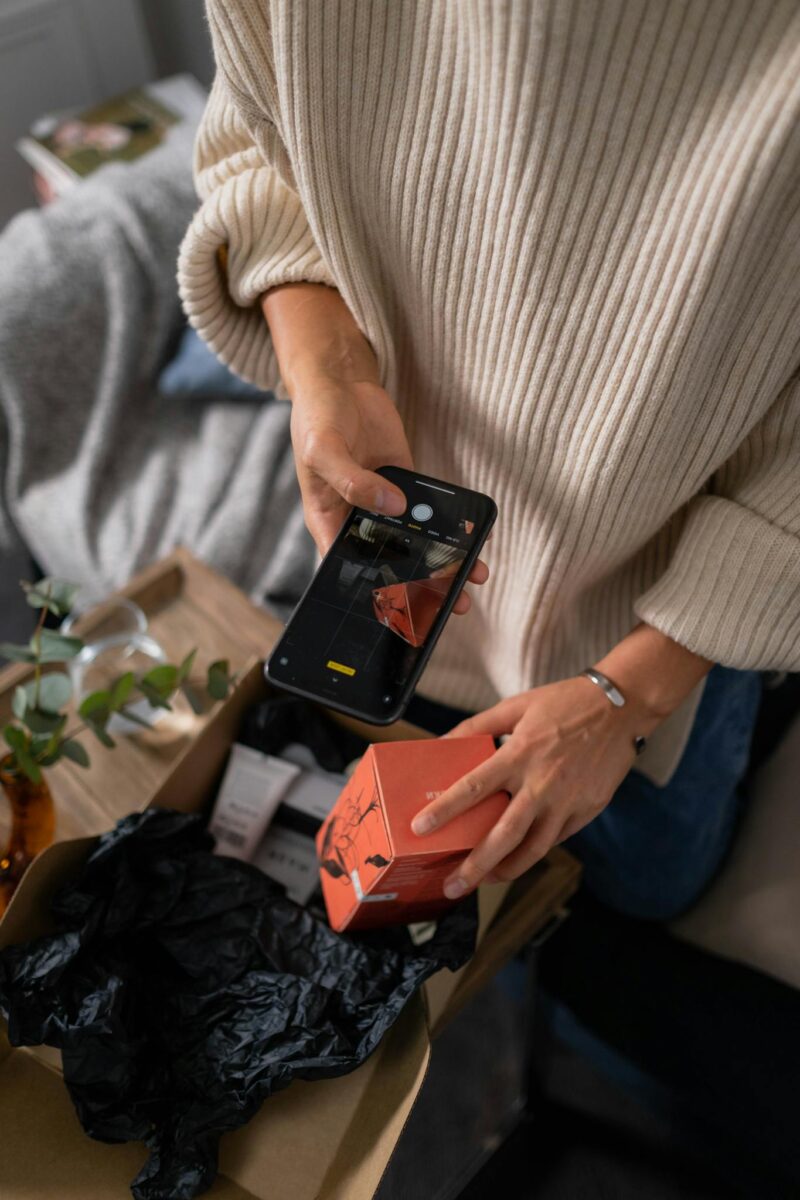 Woman Taking Pictures of Putting Items into a Cardboard Box